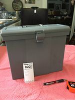 Front view of gray Rubbermaid plastic file case with locking latch and handle on top, placed on pink textured fabric.