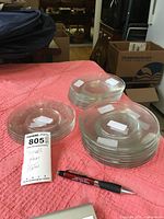 Photo showing three distinct stacks of small clear glass plates, two of the stacks appear to be plain clear plates and one stack with etched leaf designs.