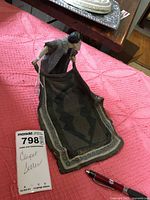 Metal sculpture of a man holding a carpet placed on a pink textured fabric background, with a pen for scale and the lot card titled 'Carpet Seller'.