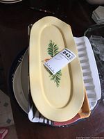 Yellow oval ceramic tray with leafy design and auction tag on top