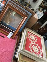 Lot of seven assorted wooden frames stacked on a pink quilted surface, some with framed lace floral textile art, others empty or with glass only.
