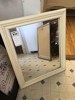 White framed mirror leaned against a kitchen floor showing full front reflective surface and frame size.