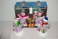 Photo showing both glass snowman figurines in front of their boxes, highlighting packaging and overall item condition