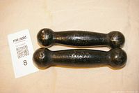 Two vintage cast iron hand weights laying side by side on a beige surface with a MaxSold lot card showing the lot number 8.