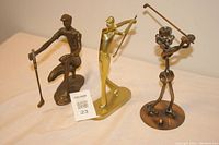 Photo of three metal golfer statues in varying styles and poses, showing front view