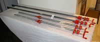 Photo of four metal bar clamps laid out on a flat surface, two long and two shorter clamps with red tightening handles.