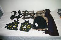 Lot arranged on a white surface showing 4 pairs of black rubber non-slip ice shoe covers with yellow studs alongside 4 hoodies including one camouflage hoodie.