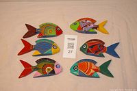 Set of six hand-painted wooden fish displayed on a light surface, each about 5 inches long, showing vibrant multicolor patterns and detailed painting.