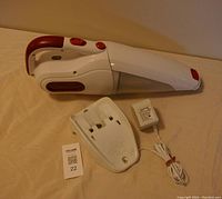 Handheld Black & Decker vacuum with detachable front nozzle, charging dock, and power adapter arranged on a surface.