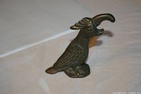 Full side view showing entire brass parrot bottle opener with textured feather patterns and curved beak opened for bottle opening function.