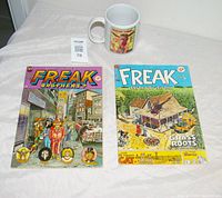 Photo showing front covers of two Freak Brothers comic books and Freak Brothers mug on a white cloth background.