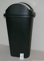 Front view of the black plastic garbage can showing its tapered rectangular shape and handle on lid.