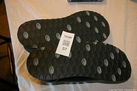 Photo showing the outsole of the shoes with oval tread pattern and attached lot tag.