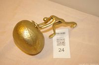 Gold-colored metal sculpture with a figure pushing a spherical boulder, photo taken to show angle and detail