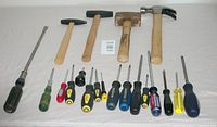 Photo showing 4 hammers and 14 screwdrivers laid out on a white surface. Hammers include claw, sledge, cross-peen, and small hammers with wooden handles. Screwdrivers vary in handle color and type, mostly flathead and Phillips.
