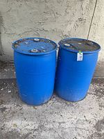 Two blue plastic 55 gallon water barrels outdoors, showing dirt and wear on lids and lower areas.