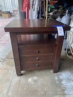 Front view of the wooden bedside table showing three drawers with metal handles and an open shelf.