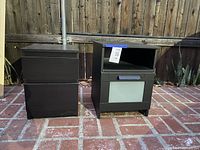 Photo of two black bedside tables with different drawer configurations, against a wooden fence on a brick patio.
