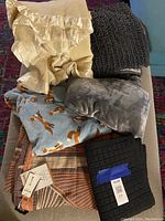 Full view of the lot showing assorted blankets and throws piled together including cream fleece, fox print fleece, grey plush, and black textured throw.