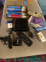 Photo showing multiple SodaStream CO2 canisters, assorted cleaning cloths, Bissell vacuum accessories, power adapter, and Braava robot mop charger base on a couch.