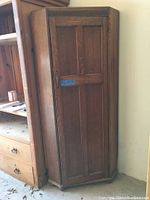 Oak corner cabinet shown closed, displaying wood panel door with molded details and overall triangular corner shape