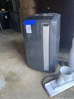Gray DeLonghi portable air conditioner showing front and side panels in a garage setting.