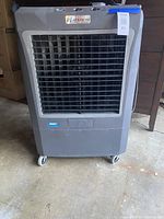 Front view of gray Hessaire evaporative cooler showing front vent and caster wheels.