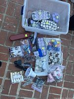 Plastic bin with multiple hairstyling tools including curlers, rollers, combs, and clips arranged on brick floor