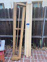 King size wooden bed frame parts leaning against a fence outdoors, showing side rails and slats.