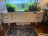 Front view of the white Mid Century Modern style office cabinet with drawers and central sliding doors, holding a fish tank on top.