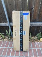 Box sealed with Amazon Prime tape standing vertically against a wooden fence, partially damaged packaging visible.