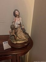 Porcelain sculpture of a gypsy mother with three children seated on a wooden base seen from front and side angles.