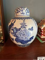 Front view of blue and white ceramic ginger jar with peony and butterfly design and lid with blue cloud motifs