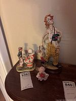 Two clown figurines, smaller elephant figurine on wooden table against wall