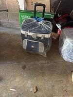 Portable Igloo cooler wrapped in plastic with telescoping handle extended, placed on concrete floor in a garage.