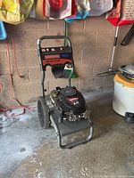 Front and side view of the Craftsman gas pressure washer in a garage setting, showing the engine, wheels, and handlebar with controls