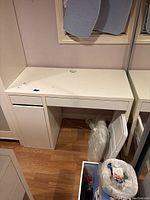 Full view of white laminate desk showing top, drawers and cabinet, along with surrounding floor and wall area.