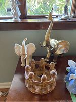 Photo showing the white elephant figurine, brass elephant figurine, and clay candle holder on a wooden dresser beside a window.
