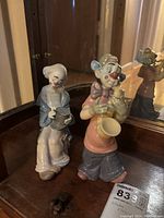 Two NAO clown ceramic figurines on a wooden surface with a mirror behind, showing distinct postures and colors of each clown.