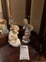 Photo showing both figurines on a wooden surface with mirror background, highlighting details of the seated girl holding a doll and the standing boy with dog.