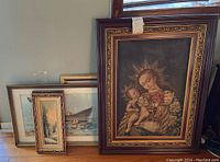 Set of five framed artworks stacked and arranged close to wall and window, showing various frame styles and sizes.