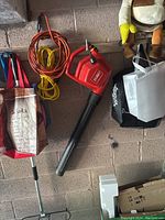 Full view of Toro electric leaf blower with attached power cord, next to two extension cords in orange and yellow, hanging on a wall.