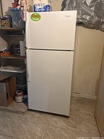 Front view of white Whirlpool refrigerator with top freezer, sticker on the door, located in basement