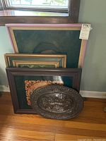 View of the four framed pictures and one metal plate arranged in a row leaning against a wall, showing colors, frames and sizes.