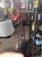 Two Black and Decker trimmers hanging on a wall shelf in the garage. The left tool is a hedgehog trimmer with a long serrated blade. The right tool is an edger with a saw cutter blade attached.
