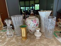 Seven vases arranged on table including porcelain Lenox floral vases, cut glass vases, and a smaller gold and green Pickard ceramic vase.
