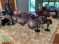Grouped image of taller purple cut to clear wine glasses with intricate floral etching, placed on tablecloth