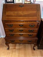 Full frontal photo of the wooden secretary desk showing four drawers, brass hardware, drop-front design, and cabriole legs.