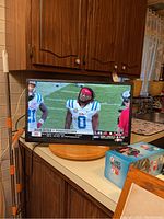 Front view of the 24-inch Vizio TV displaying a football game on screen in a kitchen setting on a round wooden stand.