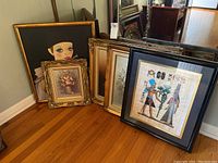 Five framed wall art pieces arranged against corner wall showing variety of art styles and frame designs.